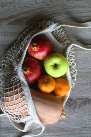 Crochet bag filled with butternut squash, pomegranates, apples and tangeriens. Top view.