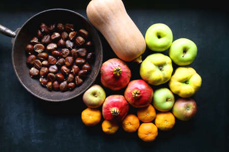 Pan with chestnuts, butternut squash and various fruit on dark background. Flat lay.の写真素材