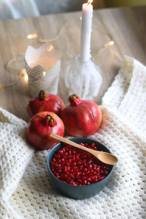 Bowl with fresh pomegranate seeds, pomegranate fruit, knitted blanket and lit candles. Hygge at home. Selective focus.の写真素材
