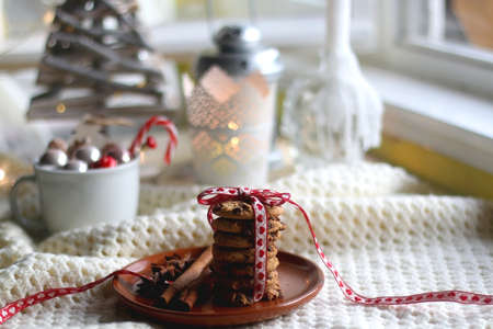 Stack of chocolate chip cookies tied with ribbon, cinnamon, anise, various Christmas decorations and lit candles. Hygge at home. Selective focus.の写真素材