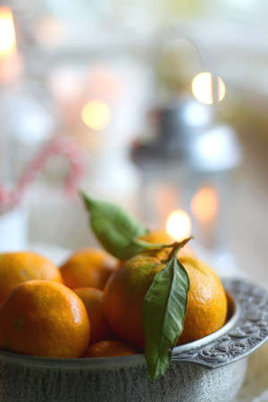 Silver bowl filled with fresh tangerines, various Christmas decorations, lit candles and soft blanket. Hygge at home. Selective focus.の写真素材