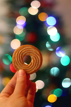 Holding a cookie in front of a Christmas tree. Selective focus.の写真素材