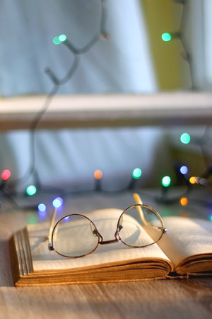 Open book and reading glasses on the table. Colorful bokeh lights in the background. Selective focus.の写真素材