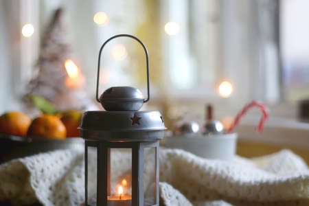 Silver bowl filled with fresh tangerines, various Christmas decorations, lit candles and soft blanket. Hygge at home. Selective focus.の写真素材