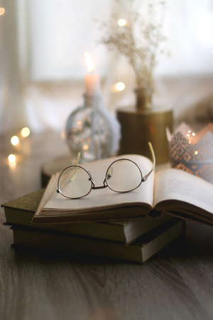Stack of vintage books, reading glasses, candles and flowers. Hygge at home. Selective focus.の写真素材