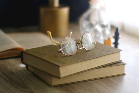 Old books, reading glasses, vintage chess pieces, lit candle and vase with gypsophila flowers. Dark academia concept. Selective focus.の写真素材