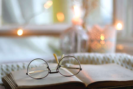 Open book and reading glasses. Candles and fairy lights in the background. Selective focus.の写真素材