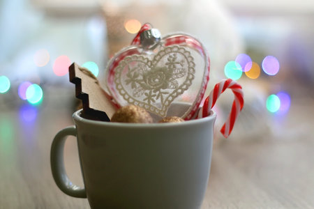 Mug filled with various Christmas ornaments, lit candles and colorful bokeh lights in the...