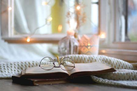 Open book and reading glasses. Candles and fairy lights in the background. Selective focus.の写真素材