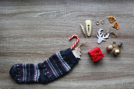 Wool stocking with small presents and Christmas decorations on wooden background. Flat lay.の写真素材
