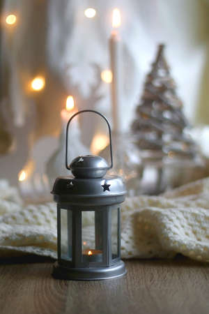 Candle holder with lit candle, reindeer and Christmas tree figurines and soft blanket. Hygge at home. Selective focus.の写真素材
