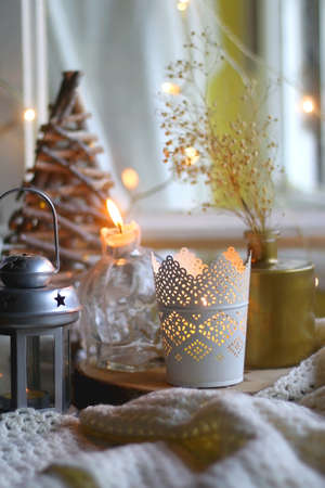 Various Christmas decorations in neutral colors, soft knitted blanket and lit candles. Selective focus.の写真素材