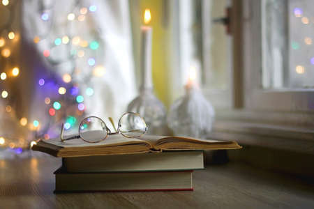 Open book and reading glasses with candles and colorful bokeh lights in the background. Selective focus.の写真素材