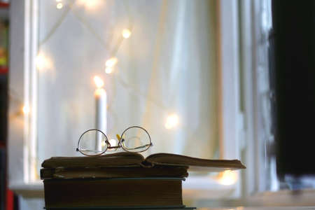Open book and reading glasses. Candles and fairy lights in the background. Selective focus.の写真素材