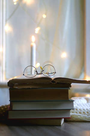 Open book and reading glasses. Candles and fairy lights in the background. Selective focus.の写真素材