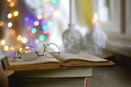 Open book and reading glasses with candles and colorful bokeh lights in the background. Selective...