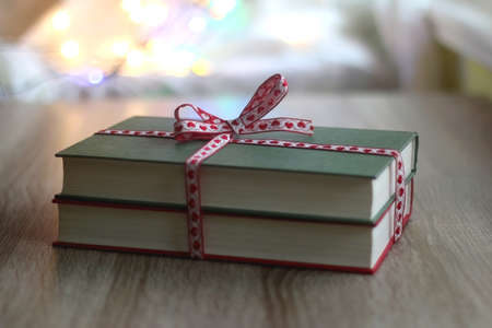 Two hardcover books wrapped with festive ribbon. Colorful Christmas lights in the background. Giving books for Christmas. Selective focus.の写真素材