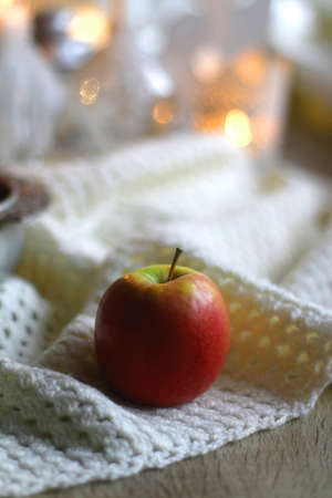 Bowl of apples and soft blanket with lit candles and Christmas decorations in the background. Selective focus.の写真素材
