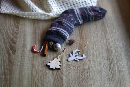Wool stocking filled with Christmas ornaments, cinnamon stick and candy cane. Cozy soft blanket in the background. Selective focus.の写真素材
