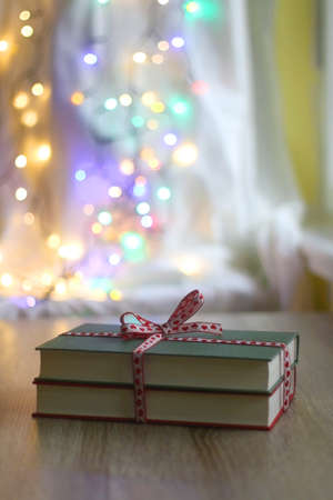 Two hardcover books wrapped with festive ribbon. Colorful Christmas lights in the background. Giving books for Christmas. Selective focus.の写真素材