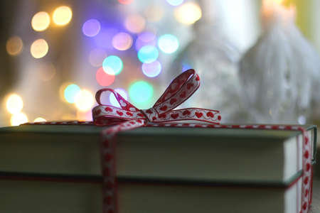 Two hardcover books wrapped with festive ribbon. Colorful Christmas lights in the background. Giving books for Christmas. Selective focus.の写真素材