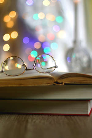 Open book and reading glasses with candles and colorful bokeh lights in the background. Selective focus.の写真素材