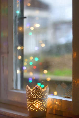 Lit candles in the window sill. Colorful bokeh lights reflected in glass. Selective focus.の写真素材