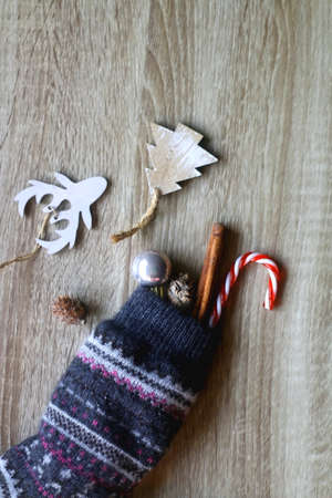 Wool stocking filled with small Christmas ornaments, cinnamon stick and candy cane. Wooden...