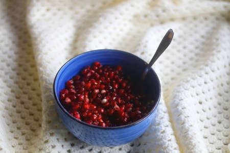 Bowl of pomegranate seeds and soft knitted blanket. Selective focus.