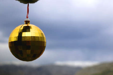 Hand in a mitten, holding golden Christmas bauble. Snowy mountain in the background. Selective focus.の写真素材