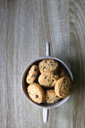 Ceramic bowl filled with chocolate chip cookies on wooden table. Flat lay.
