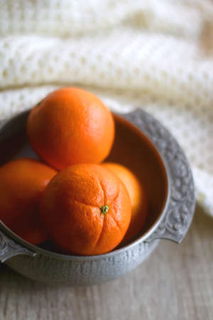 Silver bowl filled with fresh oranges and soft knitted blanket on wooden background. Selective focus.の写真素材