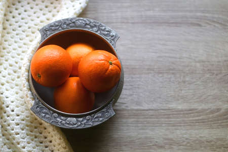 Silver bowl filled with fresh oranges and soft knitted blanket on wooden background. Selective...