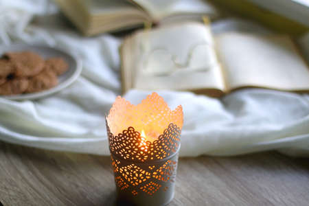 Lit candle, open books, reading glasses and plate of gluten free cookies on the table. Hygge at home. Selective focus.の写真素材