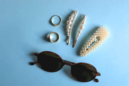 Round sunglasses, pearl hair clips and gold rings on bright blue background. Flat lay.の写真素材