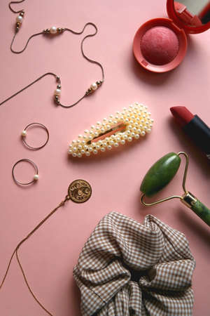 Pearl and gold jewelry, various hair accessories, make up products and jade roller on pale pink background. Flat lay.の写真素材