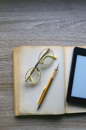 Open book, reading glasses, golden mechanical pencil and e-reader device on the table. Top view.の写真素材