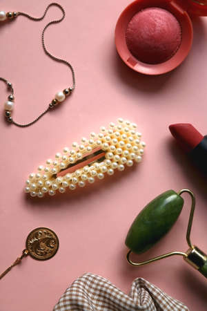 Pearl and gold jewelry, various hair accessories, make up products and jade roller on pale pink background. Flat lay.の写真素材