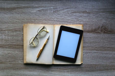 Open book, reading glasses, golden mechanical pencil and e-reader device on the table. Top view.の写真素材