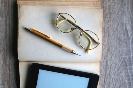 Open book, reading glasses, golden mechanical pencil and e-reader device on the table. Top view.の写真素材