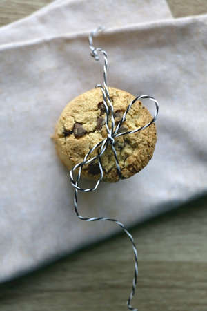 Stack of chocolate chip cookies tied with ribbon, linen napkin and wooden background. Top view.