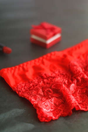 Small red giftbox, red lipstick, silver earrings and lace underpants. Valentine's Day objects on dark background. Selective focus.の写真素材
