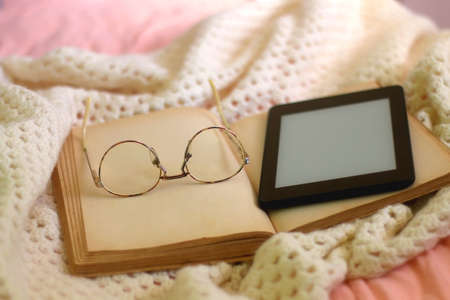 Open book, reading glasses, e-reader and soft blanket on a bed. Selective focus.の写真素材