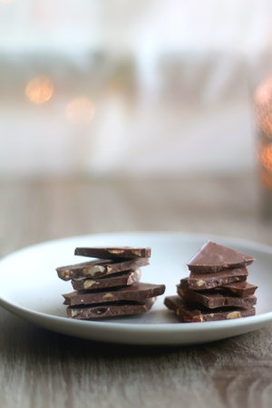 Plate with almond chocolate pieces on the table. Lit candle and bokeh lights in the background....
