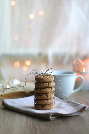 Stack of chocolate chip cookies tied with ribbon, cup of tea or coffee, open book, reading glasses,...