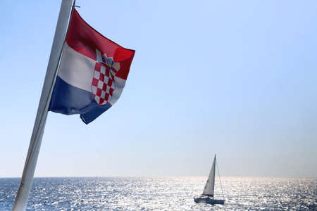 Flag of Croatia blowing in the wind. Adriatic sea, island and boats in the background.の写真素材