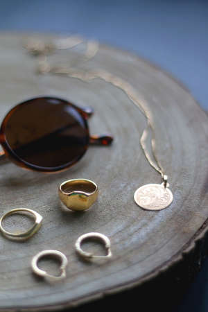 Wooden tray with round tortoiseshell sunglasses, gold necklace with pendant, hoop earrings and...
