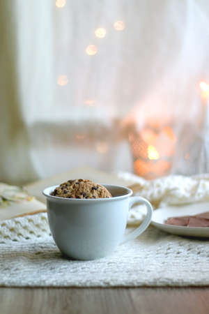 Plate with almond chocolate bar, mug with chocolate chip cookies, open book, reading glasses, soft...