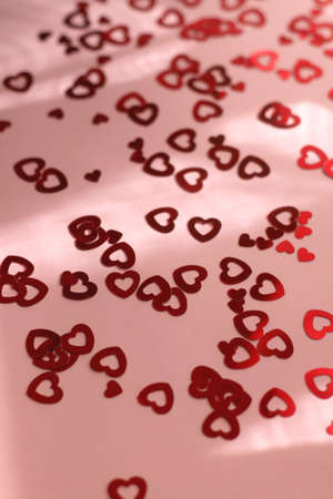 Red heart shaped confetti on pastel pink background. Selective focus.
