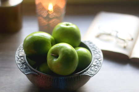 Bowl of green apples, open book, reading glasses, lit candle and flowers on the table. Selective focus.の写真素材